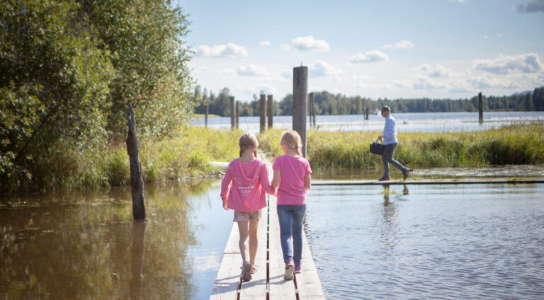 To unge jenter i rosa gensere går bortover lav bro over vannet